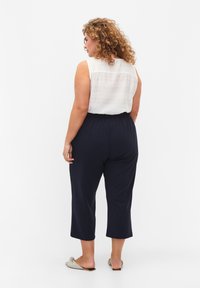 Witte mouwloze top van textuurstof, gecombineerd met marineblauwe cropped pants. De outfit heeft een elastische tailleband en een relaxte pasvorm.