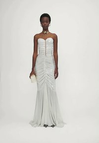 Hõbedane õhtukleit, millel on keha lähedane siluett, rütmiline tekstuur, õlgu paljastav disain ja keskne kuldne kaunistus.