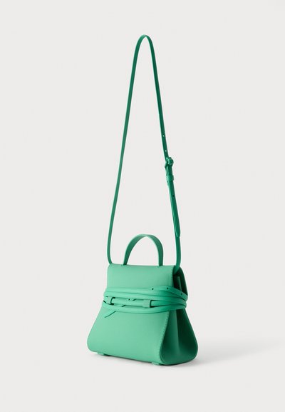 Πράσινη δερμάτινη γυναικεία τσάντα με πάνω λαβή, μακριά ρυθμιζόμενη λουρί ώμου και ζώνη που τυλίγεται γύρω, σε απλό φωτεινό φόντο.