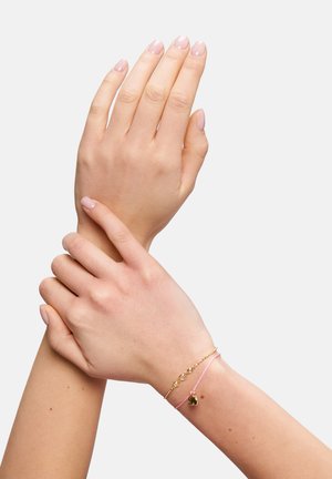Gold- und rosafarbene Armbänder mit einem Herzanhänger, geschichtet auf einem Handgelenk. Zwei Hände, die zusammengefasst sind, zeigen zarte Details und eine glatte Hautstruktur.
