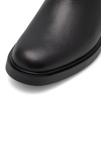 Melnas ādas zābaks ar noapaļotu purngalu, gludu tekstūru un biezu, matētu melnu zoli. Izceļas ar vienkāršu, minimālistisku dizainu bez redzamām detaļām.