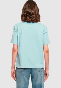 Ljusblå bomullströja med korta ärmar, avslappnad passform och enkel design på baksidan. Matchad med blå jeans med medelhög midja.