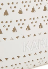White leather bag featuring cut-out triangular and circular patterns. Embroidered "KARL" logo in soft white thread. Smooth textured surface.