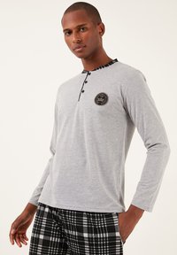 Cămașă gri cu mâneci lungi, cu un guler în carouri alb-negru, având trei nasturi și un logo circular pe piept. Pantaloni în carouri negri și gri.