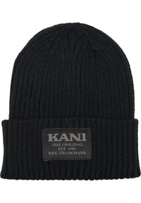 Svart strikket lue med brettet kant, med et teksturert mønster og et rektangulært merke med "KANI THE ORIGINAL EST. 1989" i hvit skrift.