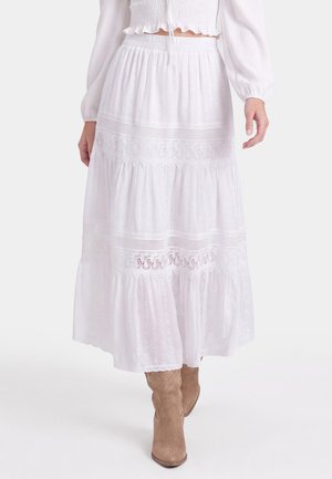 Long white tiered skirt with lace details worn with beige cowboy boots and a white long-sleeve top, shown from mid-torso to feet.