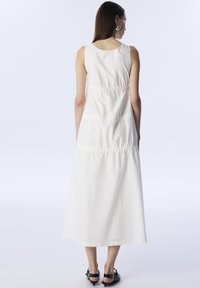 Vestido maxi blanco sin mangas con escote redondo, que presenta costuras fruncidas a lo largo de la cintura y una silueta recta y fluida.