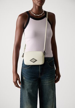 Borsa a tracolla in pelle bianca con logo a diamante, caratterizzata da una forma rettangolare elegante e una tracolla staccabile. Indossata con una canotta chiara.