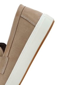 Zapato-slip beige de ante, con suela de goma blanca, forro interior marrón y costura blanca contrastante a lo largo de la costura. Diseño de puntera redondeada y plana.