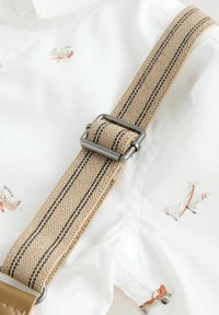 Tan suspenders with black stripes, featuring metal hardware, attached to a white shirt decorated with small airplane patterns.