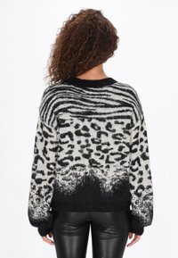 Gestreifter und gepunkteter Pullover in Schwarz-Weiß, der eine Mischung aus Streifen und Leopardenflecken zeigt, mit einem abgestuften schwarzen Saum und strukturierten Ärmeln.