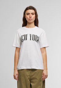 Bílý bavlněný tričko s krátkými rukávy a kulatým výstřihem, na kterém je výrazný černý nápis "NEW YORK" přes hruď.