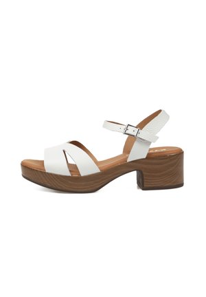 Sandalia blanca de cuero con punta abierta, tacón de bloque de madera y correa ajustable en el tobillo con hebilla plateada.