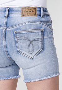 Svetlo modri denim kratke hlače z razfrkanim robom, z dekorativnim šivanim designom žepa in umetnim usnjenim oznako na pasu.