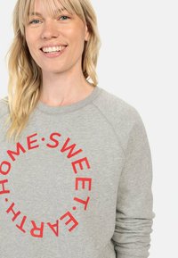 Grijze sweatshirt met rode cirkelvormige tekst "HOME SWEET EARTH." Heeft een ronde hals en raglanmouwen, gemaakt van zachte stof.