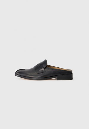 Zapatilla mule de cuero negro con suela plana, punta redondeada y una tira ancha en la parte superior con un discreto logotipo y detalles de costura.