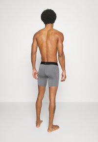 Sive bokser hlače s črnim pasom, oprijet dizajn, gladka tekstura in dolžina do kolen. Vidni šivi na straneh.