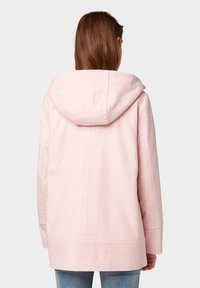Abrigo rosa claro con capucha y corte relajado, hecho de una tela suave. Presenta detalles en las costuras y bolsillos laterales, con un diseño simple y sin adornos.