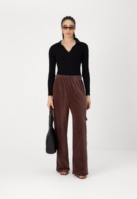 Μαύρη ριμπ μακριά μπλούζα με γιακά, συνδυασμένη με καφέ βελουτέ παντελόνι σε φαρδιά γραμμή που διαθέτει πλαϊνές τσέπες. Αξεσουάρ περιλαμβάνουν γυαλιά ηλίου και τσάντα.