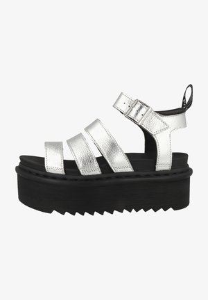 Sandalias de plata con tiras, tres bandas metálicas, hebilla ajustable, suela de plataforma negra y patrón en zigzag texturizado en la parte inferior.