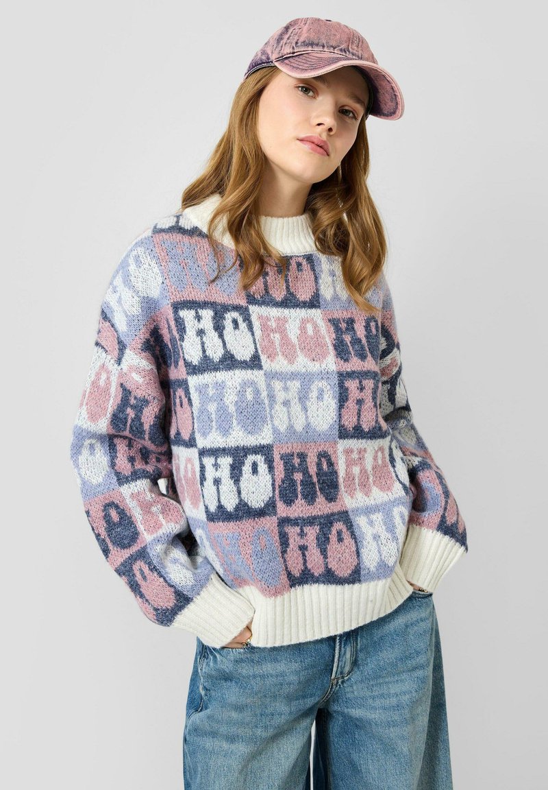 Pull en tricot avec un motif à carreaux dans des tons de rose, bleu et blanc, avec un col et des poignets côtelés crème. Associé à une casquette rose.