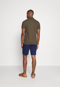 Olivengrønn polo skjorte med korte ermer, sammen med blå shorts. Brune sandaler med stropper. Enkelt, teksturert stoffdesign, uten mønstre.