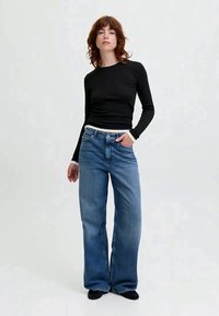 Črn dolg rokav vrh z belimi manšetami, v kombinaciji s svetlo modrimi širokimi hlačami. Hlače imajo klasičen pet-pocket oblikovanje in gumbasto zapiranje.