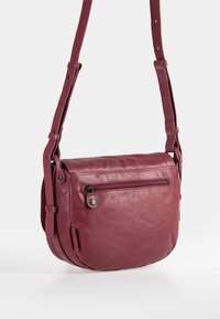 Bordeauxroter Leder-Umhängetasche mit verstellbarem Riemen, ausgestattet mit einer vorderen Reißverschlusstasche und glatter Textur. Kompakte, abgerundete Form.