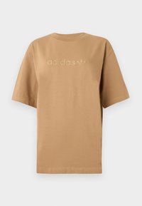 Smeđa pamučna majica s kratkim rukavima i okruglim izrezom. Sadrži izbočeni logotip "adidas" i trofej emblema u usklađenoj nijansi.