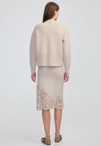 Maglione beige lavorato a maglia con un design accorciato abbinato a una gonna coordinata con dettagli in pizzo intricati all'orlo.