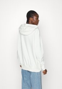 Hvit hettegenser med snor i hetta, ribbede mansjetter og søm, sammen med lyseblå jeans. Glatt tekstur, uformell oversized passform.