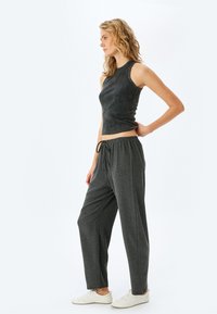 Grå cropped tanktop med en rund halsudskæring, parret med løstsiddende, mørkegrå bukser med elastisk talje og snoretræk.