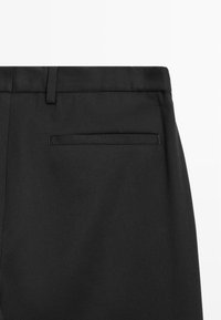 Schwarze Hose aus einem glatten, strukturierten Stoff, mit einem Bund mit Gürtelschlaufen und einer einzelnen, ungeschmückten Gesäßtasche.