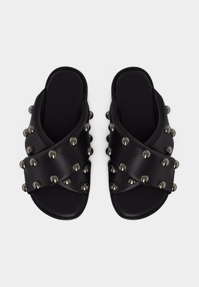 Sandales plates noires avec larges brides croisées ornées de clous métalliques ronds, semelle plate et design à bout ouvert, vues de dessus.
