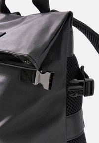 Schwarzer Rucksack mit glänzender Nylon-Oberfläche, ausgestattet mit Mesh-Details, einem umklappbaren Deckel und einem metallischen Clipschluss für zusätzlichen Nutzen.
