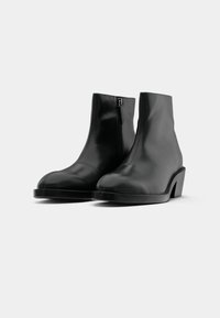 Melni potītes zābaki, kas izgatavoti no gludas ādas, ar sānu rāvējslēdzēju, noapaļotu purngalu un masīlu papēdi. Minimālistisks dizains ar elegantu siluetu.