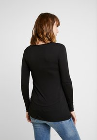 Top preto de manga longa com bainha arredondada, feito de material suave e liso. A parte de trás apresenta um design simples e um corte descontraído.