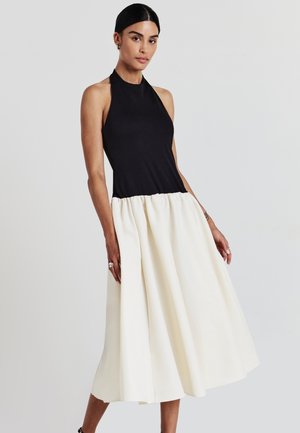 Top nero con collo a halter, con un corpino attillato che si trasforma in una gonna bianca voluminoso. Tessuto liscio e silhouette a campana, con orlo all'altezza del ginocchio.