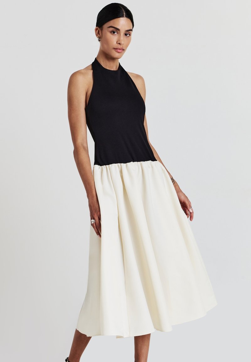 Top nero con collo a halter, con un corpino attillato che si trasforma in una gonna bianca voluminoso. Tessuto liscio e silhouette a campana, con orlo all'altezza del ginocchio.