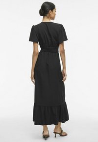 Mustmust tõusva varrukaga must maksikleit, smockitud vöökoht ja kihiline ripskrae. Valmistatud kergest kangast, millel on sile tekstuur.