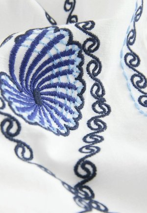 Tkanina haftowana z niebieskim wzorem muszli morskiej i ciemnoniebieskimi zawijasami na białym tle, podkreślająca szczegółowe ściegi i fakturę.