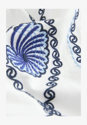 Tkanina haftowana z niebieskim wzorem muszli morskiej i ciemnoniebieskimi zawijasami na białym tle, podkreślająca szczegółowe ściegi i fakturę.