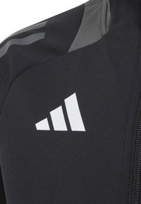 Schwarze Sportjacke mit einem auffälligen weißen Logo und drei Streifen. Glatte Textur mit grauen Akzenten auf den Schultern. Mit Reißverschluss. 