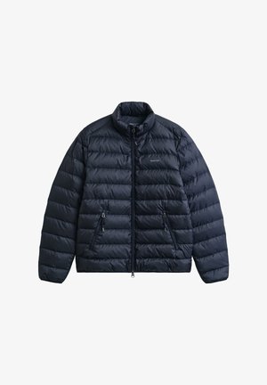 Veste matelassée bleu marine avec col montant, fermeture éclair à l'avant et deux poches latérales. Comprend un motif matelassé et un logo sur la poitrine.