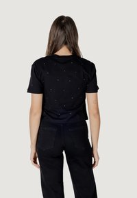 T-shirt nero a maniche corte con motivi argento sul retro, abbinato a pantaloni neri a vita alta. Texture liscia e vestibilità casual.