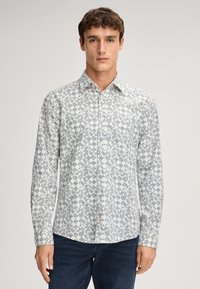 Witte overhemd met lange mouwen en een geometrisch blauw patroon, met knopen aan de voorkant en een kraag. De stof lijkt glad en lichtgewicht te zijn.