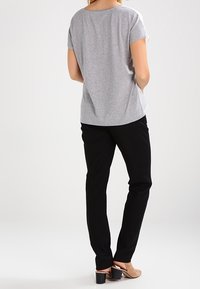 Camiseta gris de manga corta con un corte relajado, combinada con pantalones ajustados negros y zapatos de tacón bloque color beige, vista desde la parte de atrás.