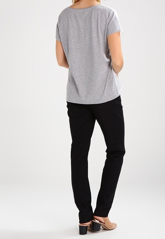 Camiseta gris de manga corta con un corte relajado, combinada con pantalones ajustados negros y zapatos de tacón bloque color beige, vista desde la parte de atrás.