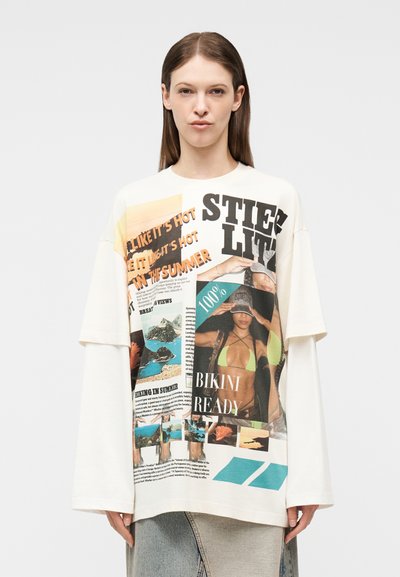 Femme portant une chemise blanche ample à manches longues avec un imprimé collage coloré sur le thème de l'été, comprenant des textes, des images d'un mannequin en bikini et des scènes de nature.