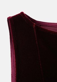 Țesătură de catifea burgundă cu un finisaj moale și texturat. Prezintă un gât rotund și un detaliu de cusătură pe umăr.